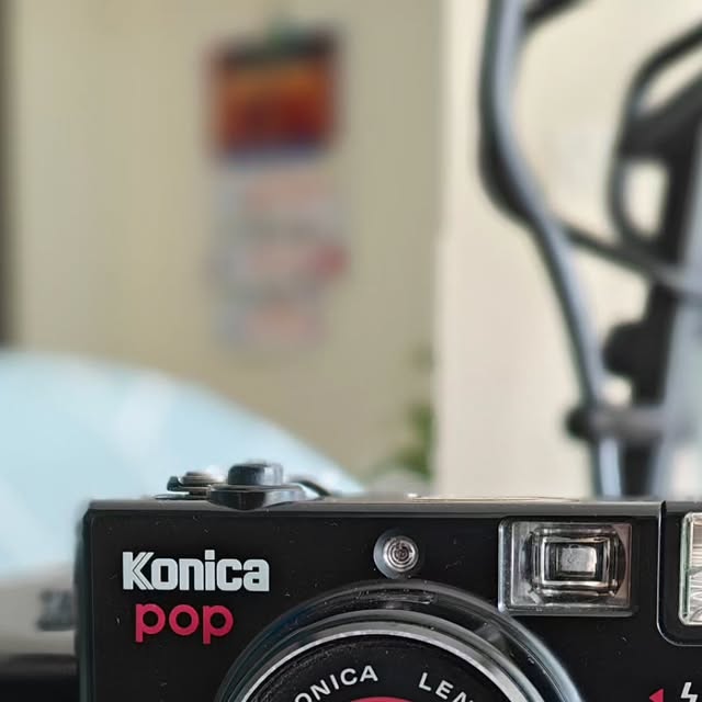 Close-up of a black Konica Pop 35mm film camera in front of a blurred room